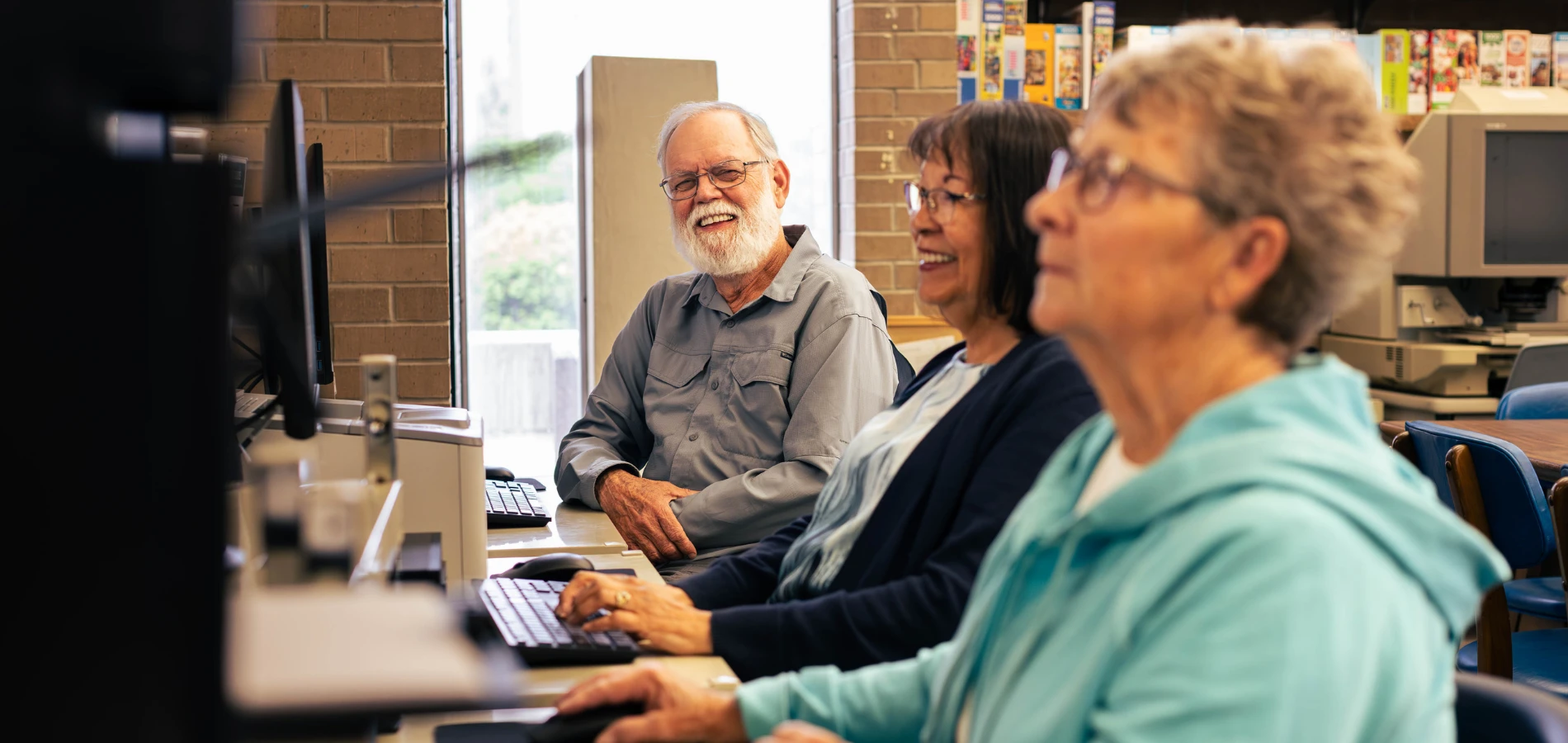 Three adults sit at a row of desktop computers. 