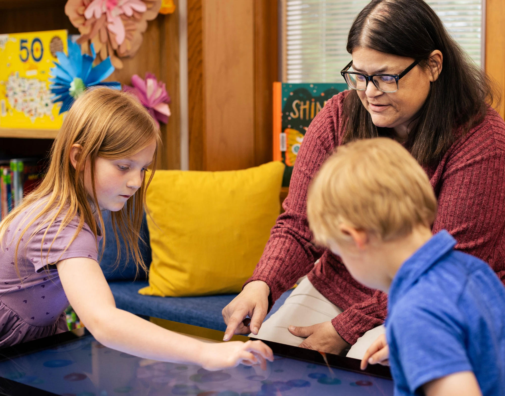 An adult and two children play a game on a large table screen.