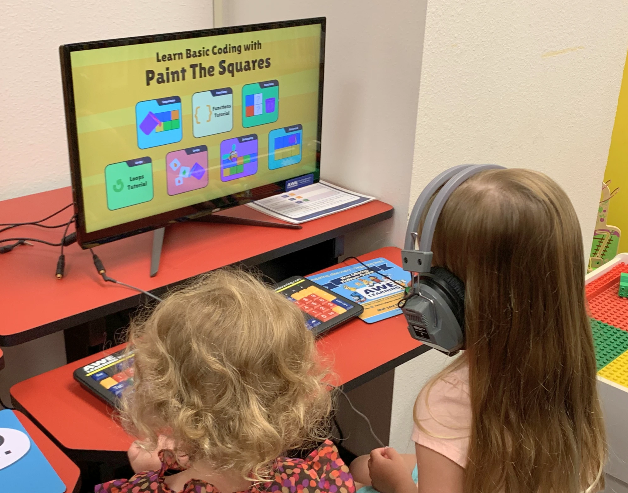 Two children sit in chairs and read a computer screen.