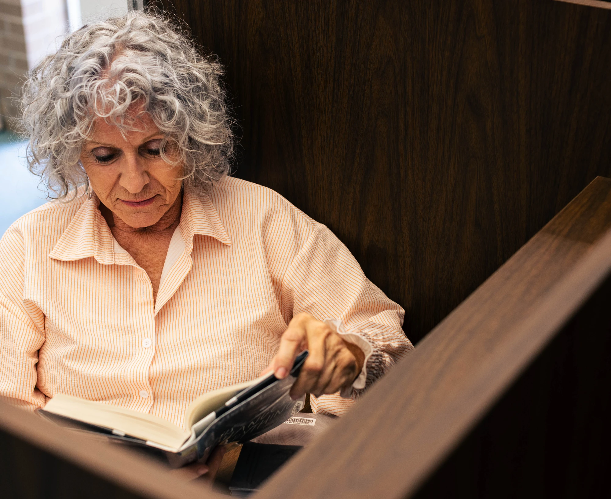 An adult with gray curly hair reads a book in a study cubicle.